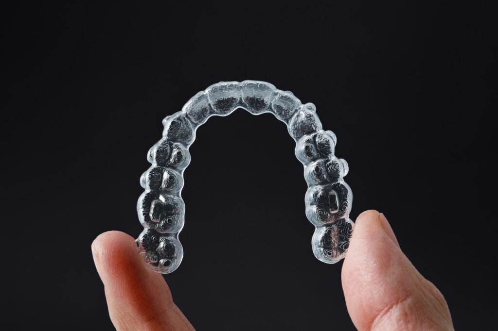 hand holding one transparent retainer on black background invisalign orthodontics concept