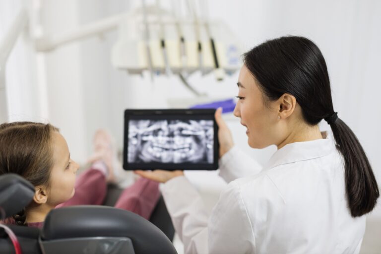 back view of smiling happy caucasian child girl visiting dentist sitting in dental chair