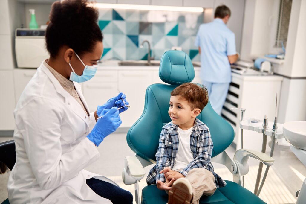 small boy talking to dentist before teeth examination at dentist s office