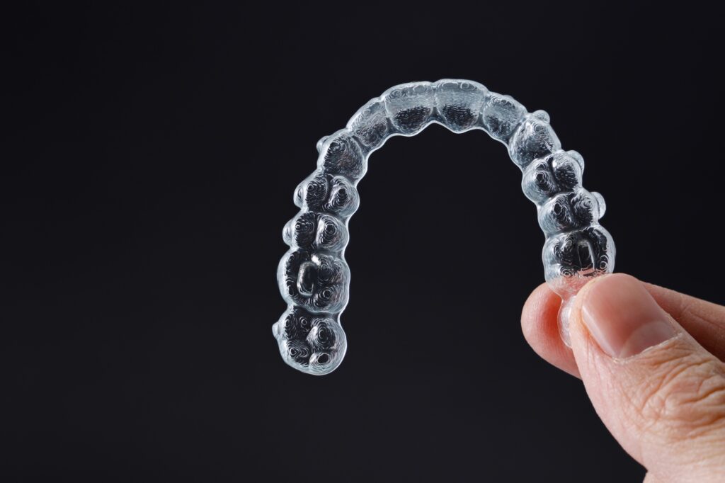 hand holding one transparent retainer on black background invisalign orthodontics concept