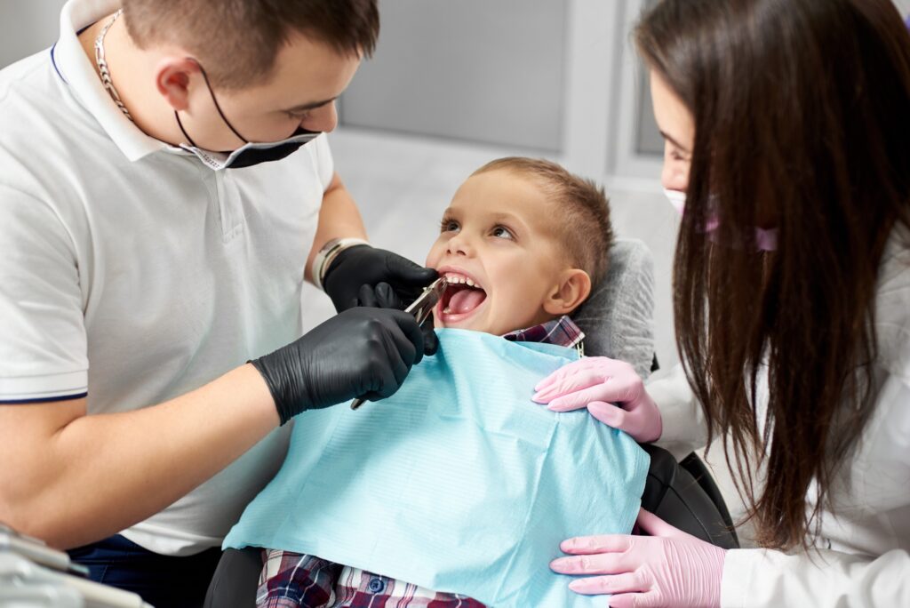 dentist and assistant pull the tooth to the baby with forceps