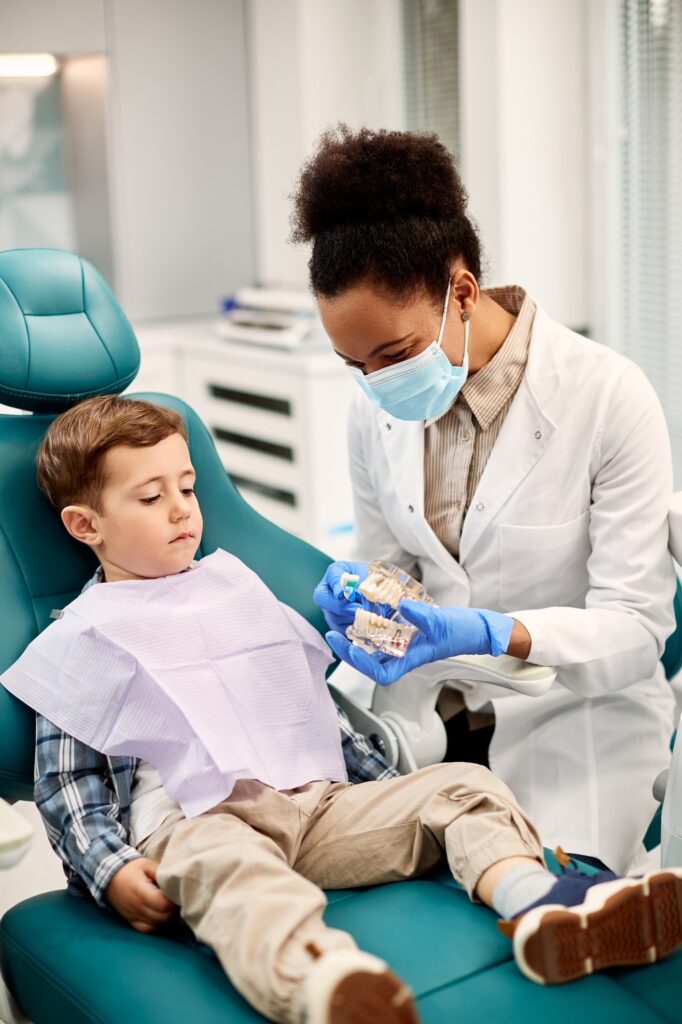 black female dentist using denture and toothbrush during appointment with child at dentist s office