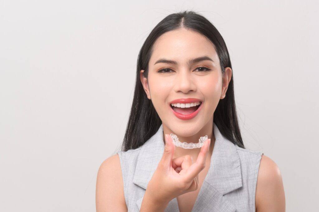 young smiling woman holding invisalign braces in studio